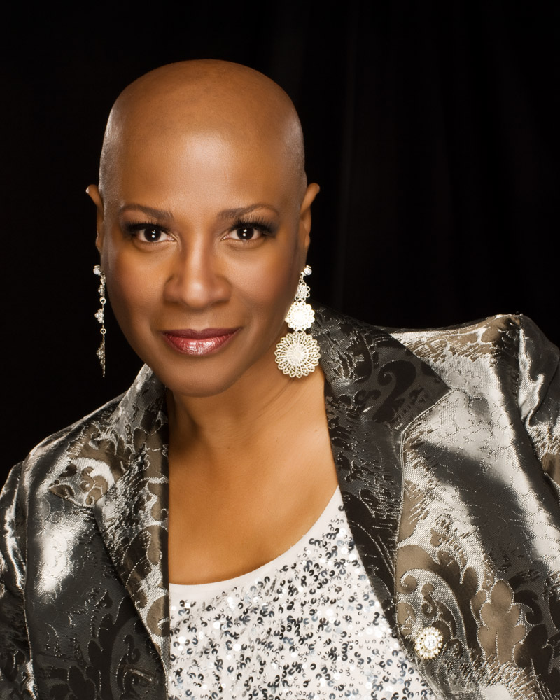 A Black woman with a shaved head looks confidently at the camera.