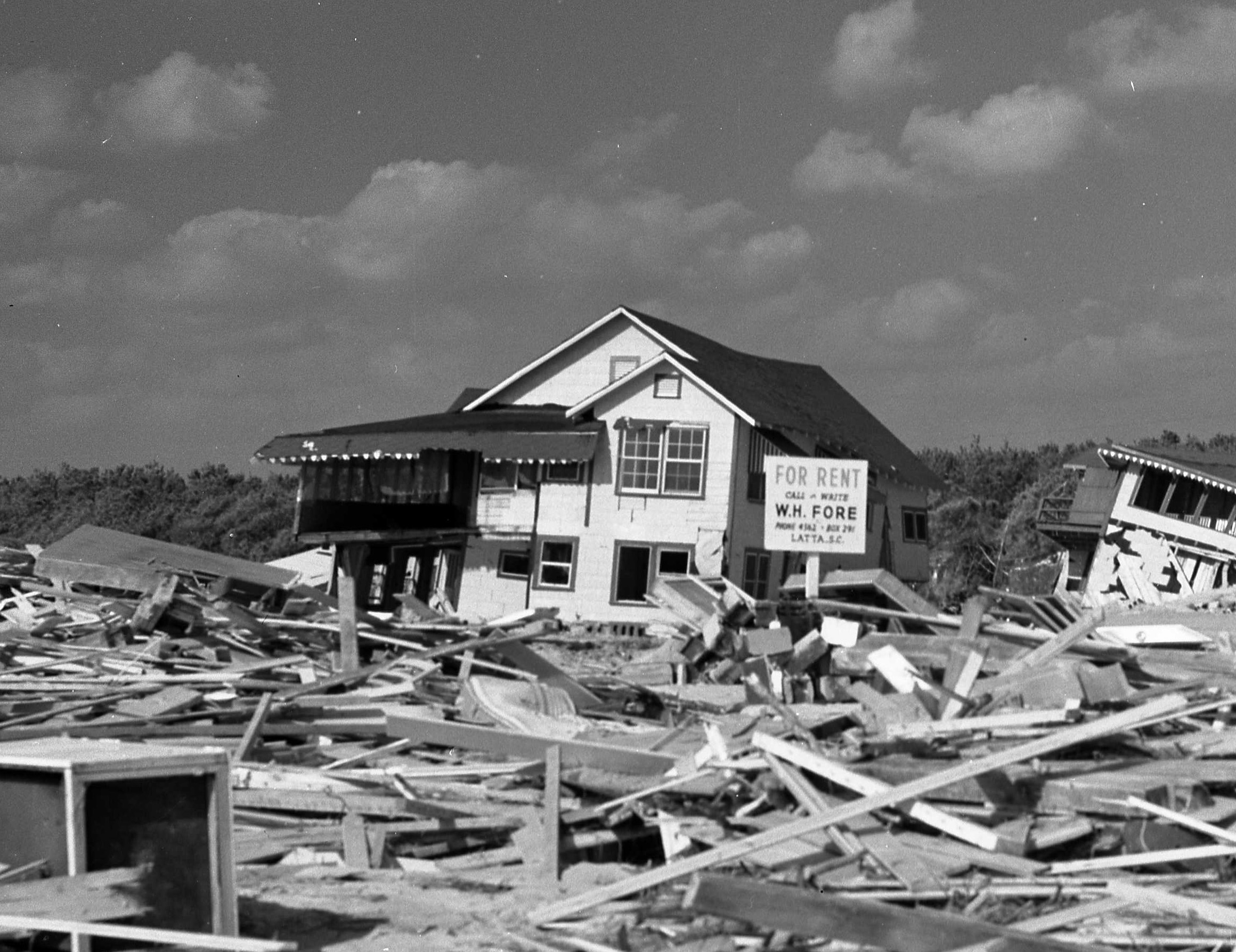 A coastal house, ruined by a hurricane, with debris covering the beach in front.