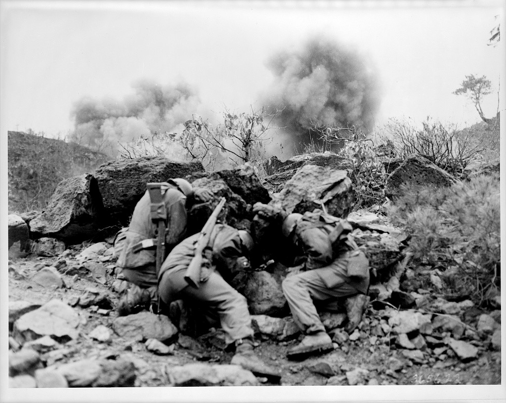 U.S. soldiers behind rocks to shield themselves from exploding mortar shells during the Korean War.
