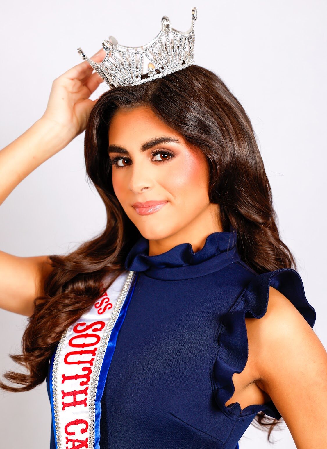 A young woman wearing a "Miss South Carolina" sash holds a silver crown on her head.