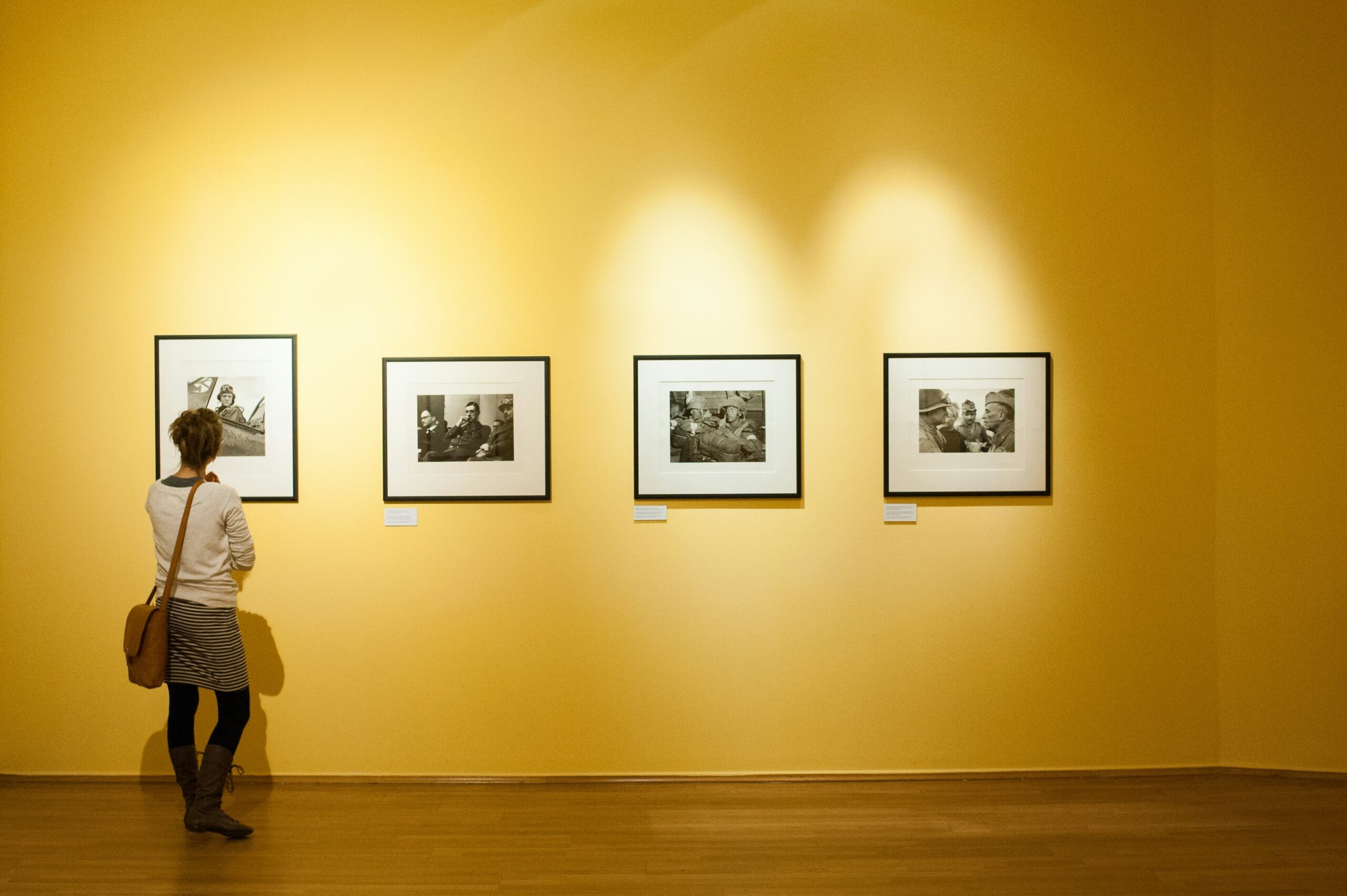 A woman stands viewing 1 of 4 black and white photographs displayed on a large yellow gallery wall.