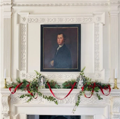 A white painted mantel, decorated with holiday greenery, featured a framed historical portrait of a man.