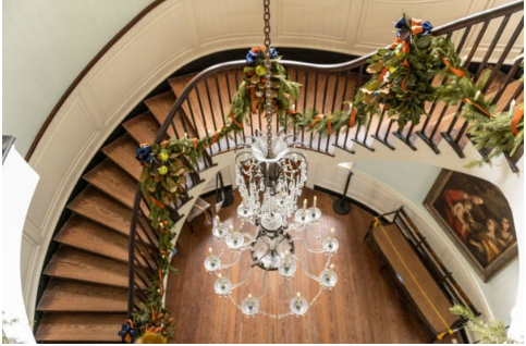 a grand wooden staircase and foyer, with a crystal chandelier, decorated with greenery