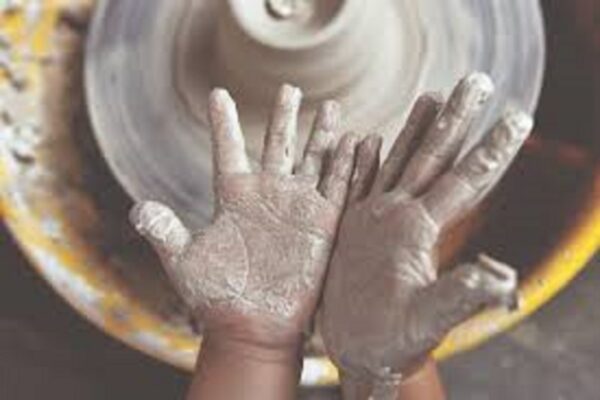 A child's hands, covered in wet clay, above a potter's wheel.