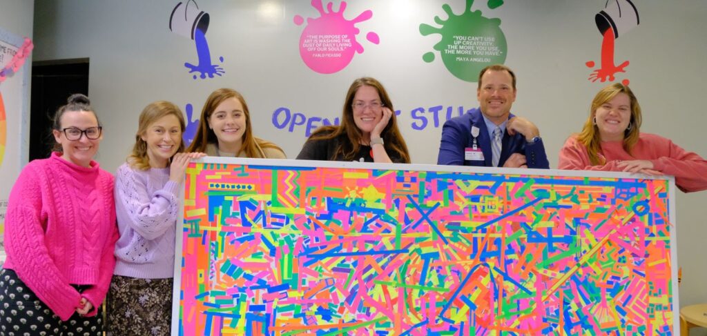 Five white women and one white man pose in front of a piece of the mural.