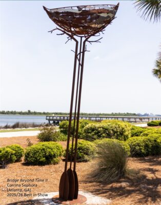 A large outdoor sculpture of brown metal. 3 oars stand on end with branches and a nest at the top.