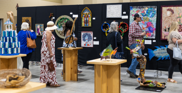 Attendees at an art show view works on pedestals and on black fabric standing panels.