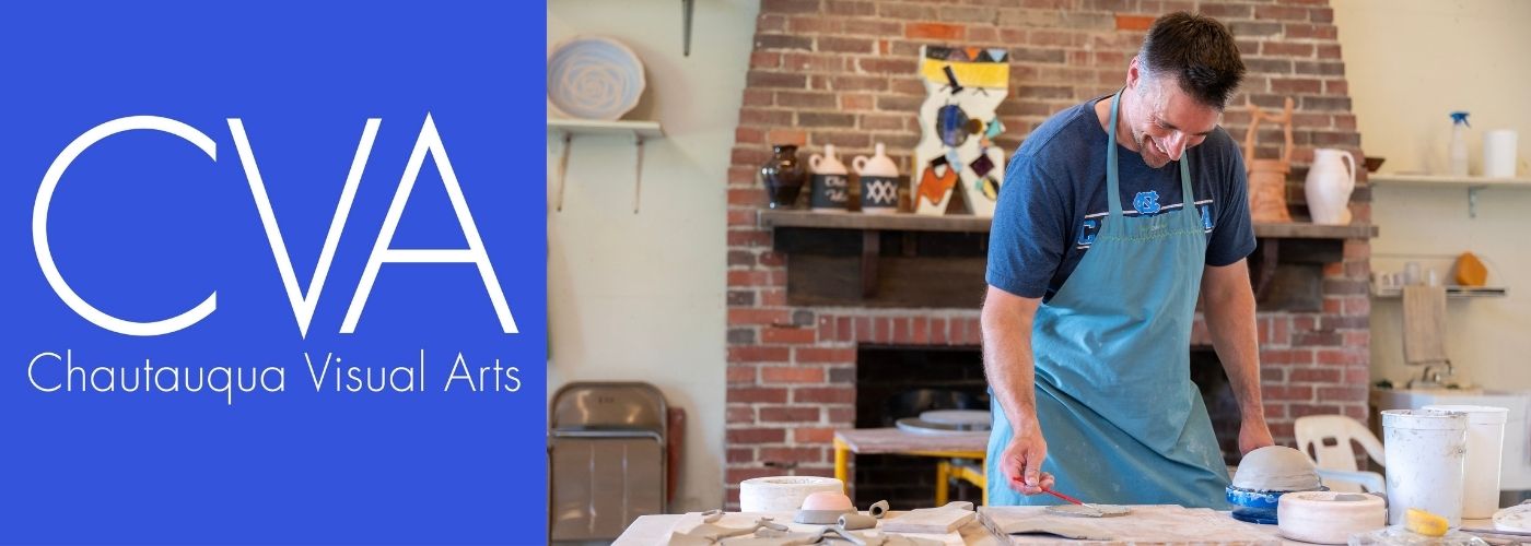 A smiling man in an apron and t-shirt works with slabs of clay on a table.