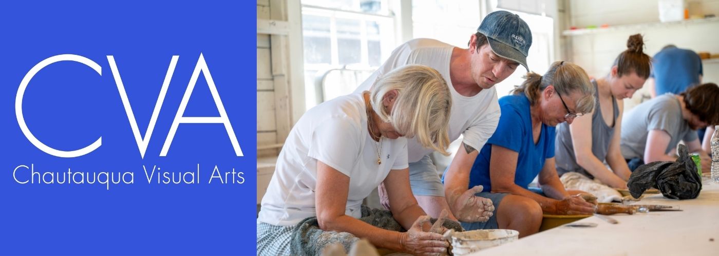 A row of adult students work on pottery wheels as an instructor leans over to advise.
