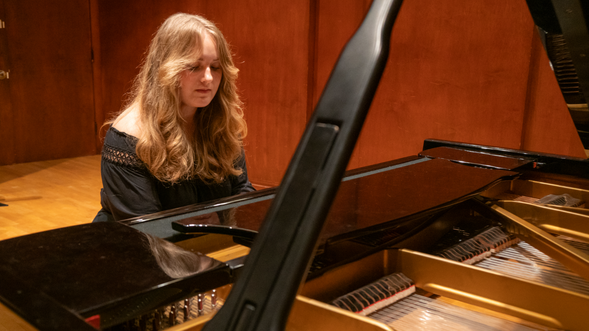 A female student playing the piano on a concert stage.