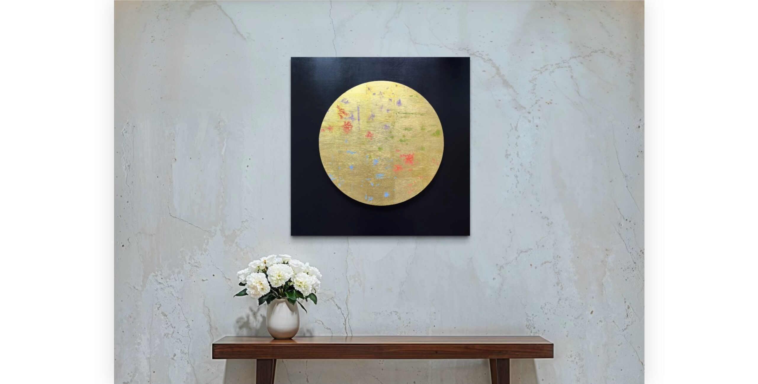 Artwork hung on a white marble wall above a table with a vase of flowers.