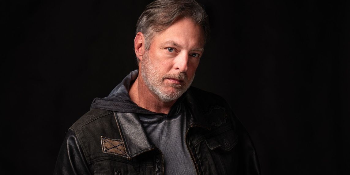 A man with graying brown hair and beard stares intently at the viewer.
