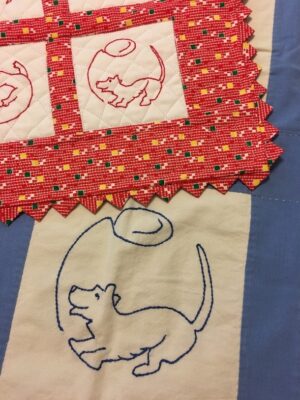 Quilted squares embroidered with a line drawing of a dog chasing a balloon.