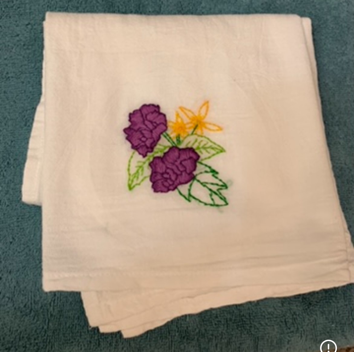 An off-white handkerchief embroidered with purple and yellow flowers with green leaves.
