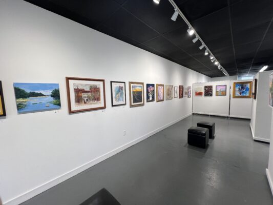 An art gallery with white walls and gray floors displays two-dimensional artworks.