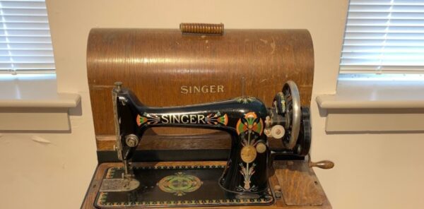 Black antique Singer sewing machine with a wooden base and cover.