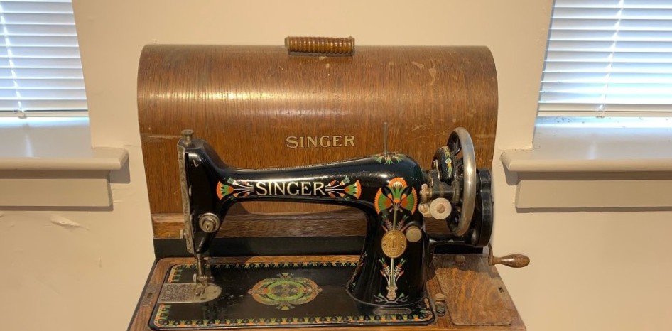 Black antique Singer sewing machine with a wooden base and cover.
