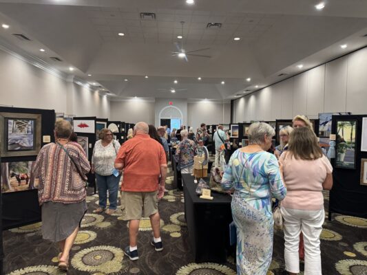 People viewing art on black panels and black tables in a ballroom.