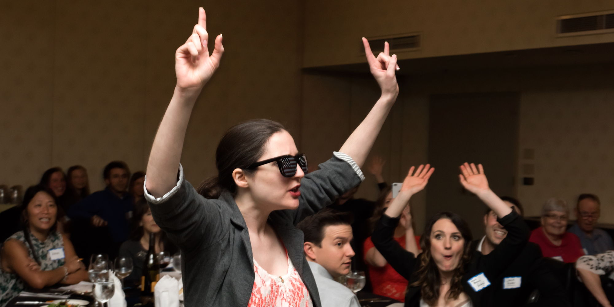 A woman in sunglasses speaks as she holds up her hands amid a seated crowd.
