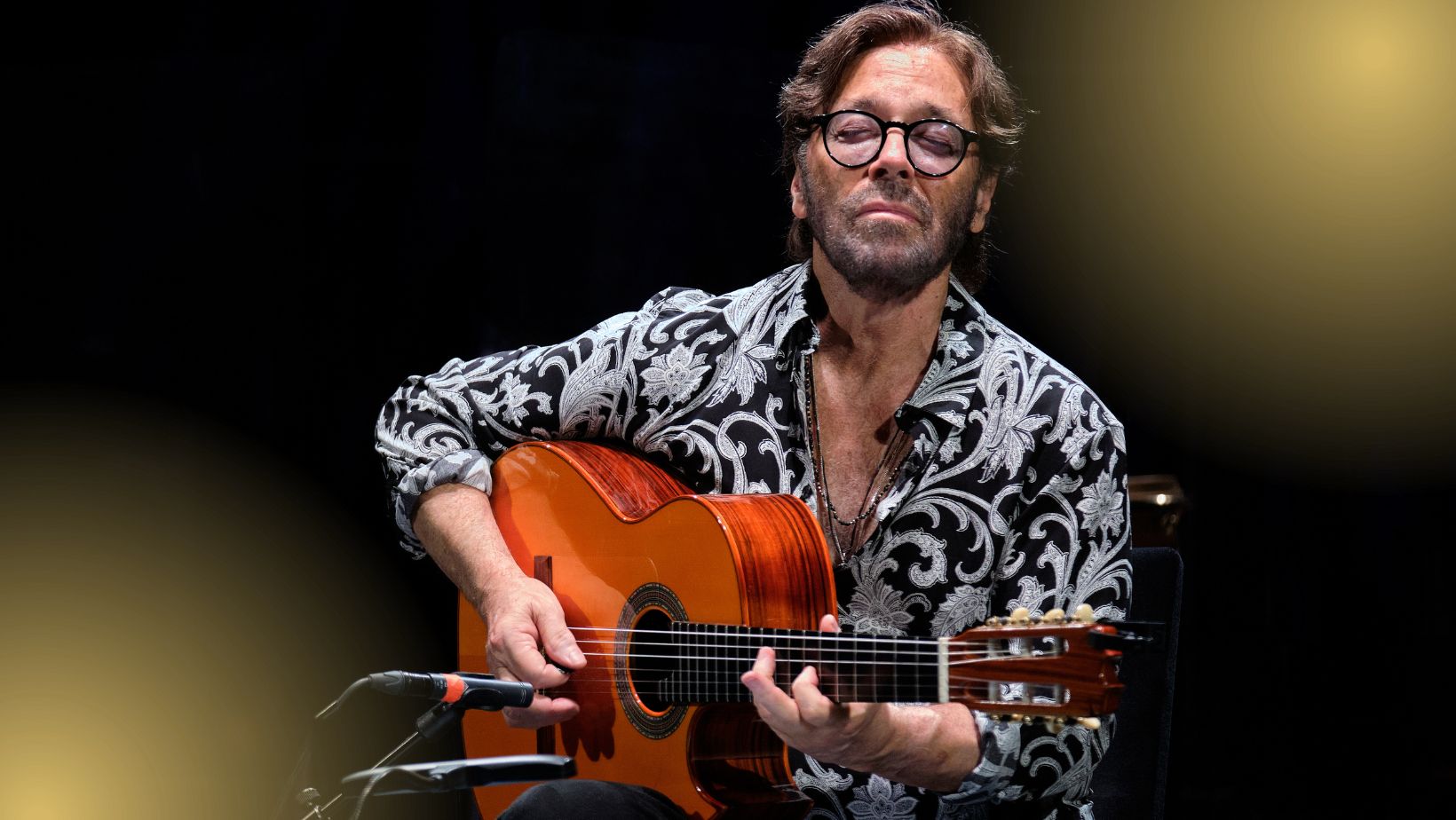 A man plays an acoustic guitar with eyes closed, onstage.