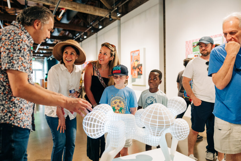 A handful of people crown around a small white sculpture.