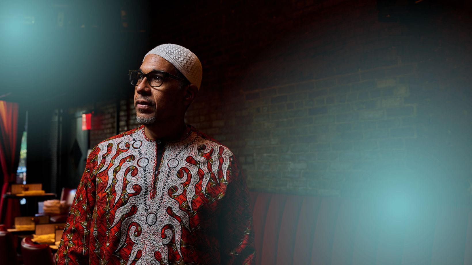 A BIPOC-presenting man in an embroidered shirt and a knit cap looks off-camera.