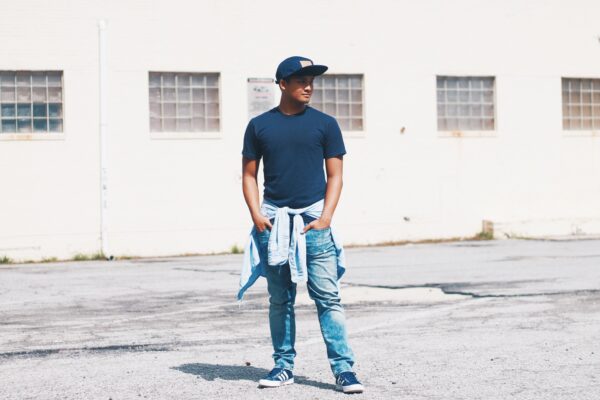 A BIPOC man wearing casual clothing stands in a concrete lot. He is looking to the side.