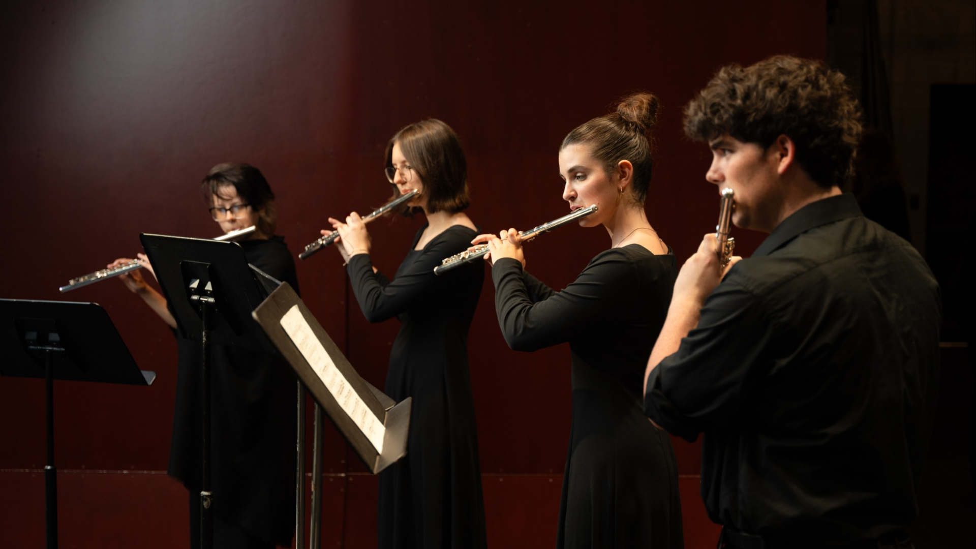 Student flute quartet performs onstage. They wear formal black concert attire.