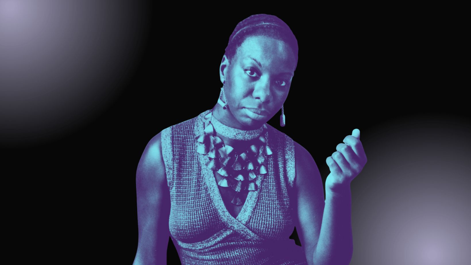 A Black woman with close-cropped hair closes one raised hand and stares strongly at the viewer.
