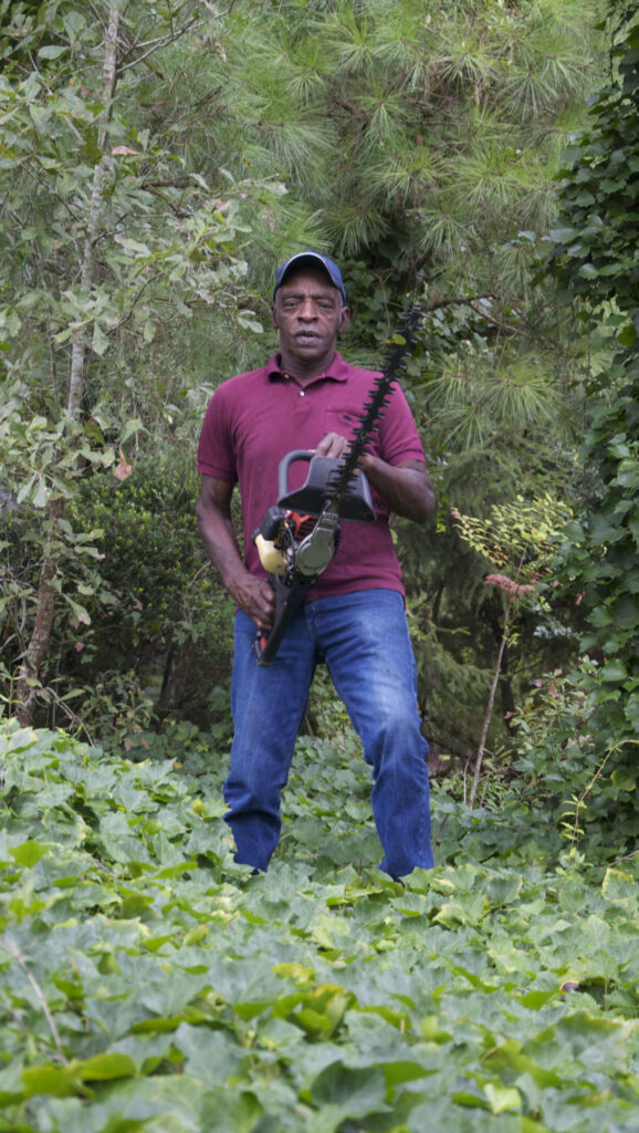 An older black man in the woods with a pruning trimmer.