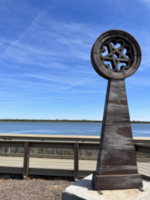 "Tin of Hearts," a large outdoor sculpture by Beau Lyday, is shown near a calm blue body of water.