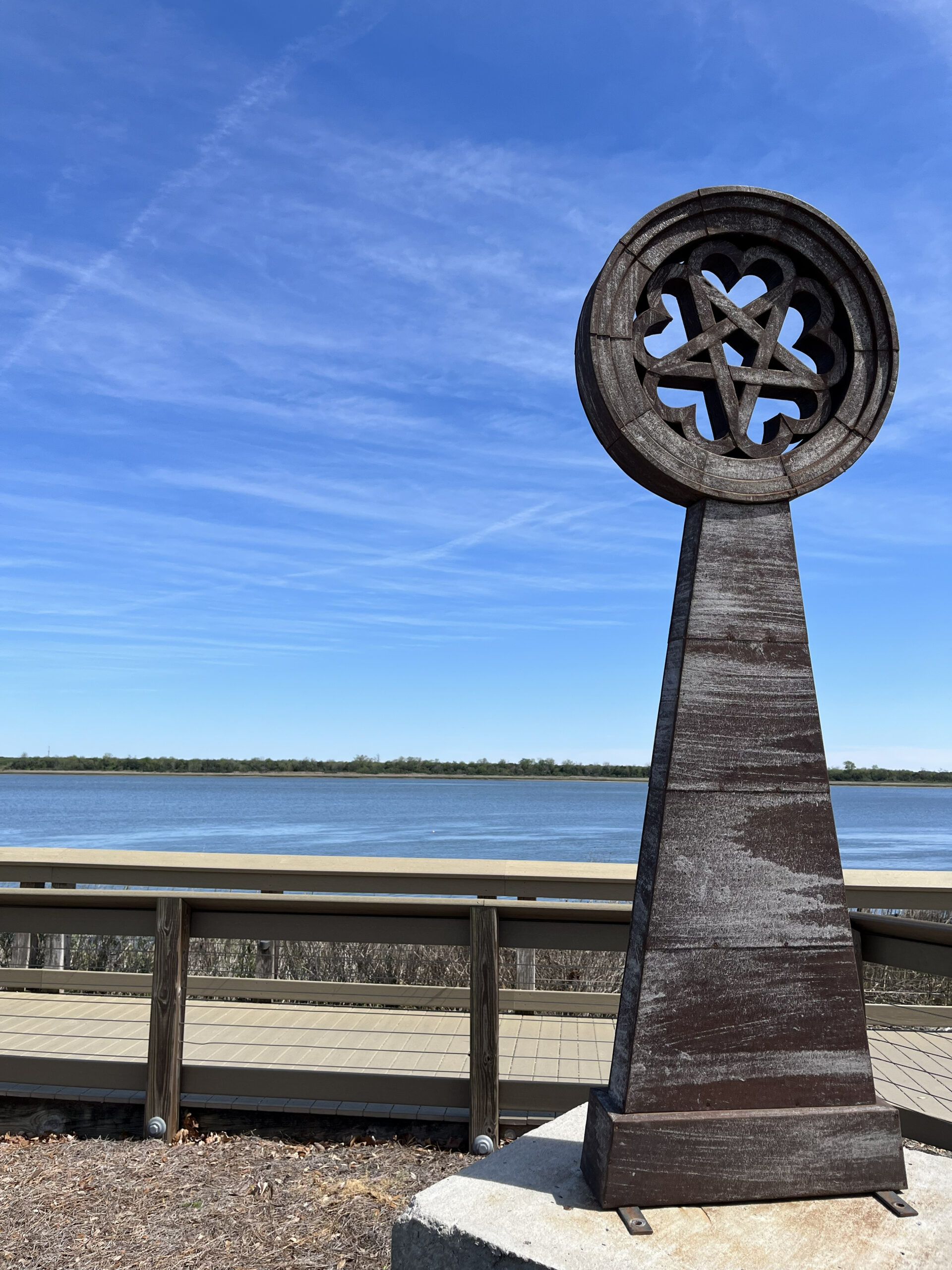 "Tin of Hearts," a large outdoor sculpture by Beau Lyday, is shown near a calm blue body of water.