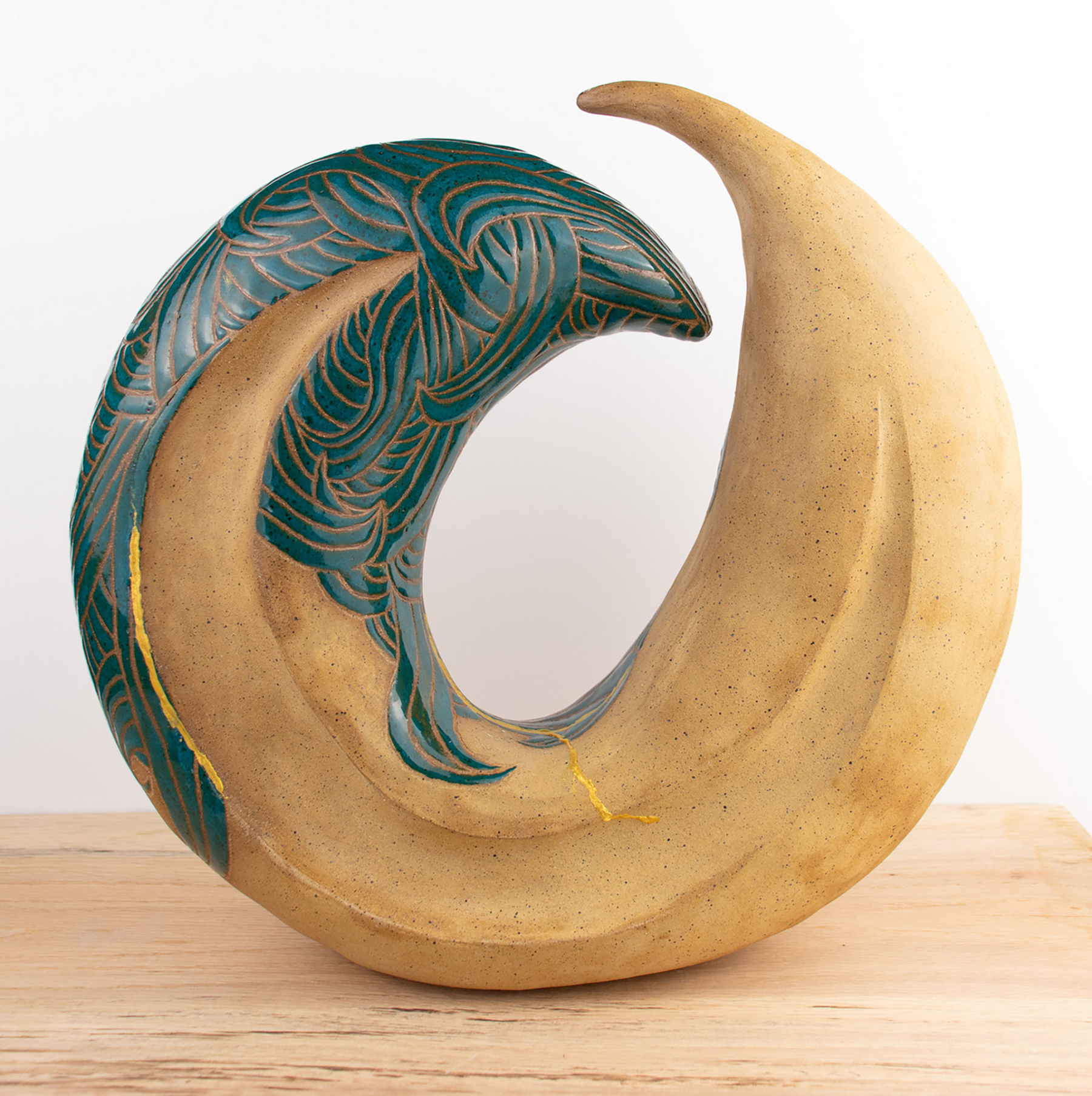 Stoneware clay sculpture forms a wave-like incomplete circle, with etched teal glazing at the crest.
