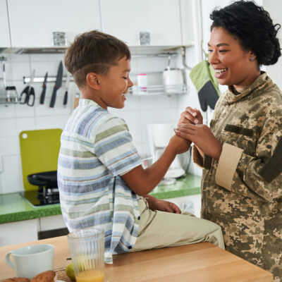 Black mother in military digi-camo holding hand of son.