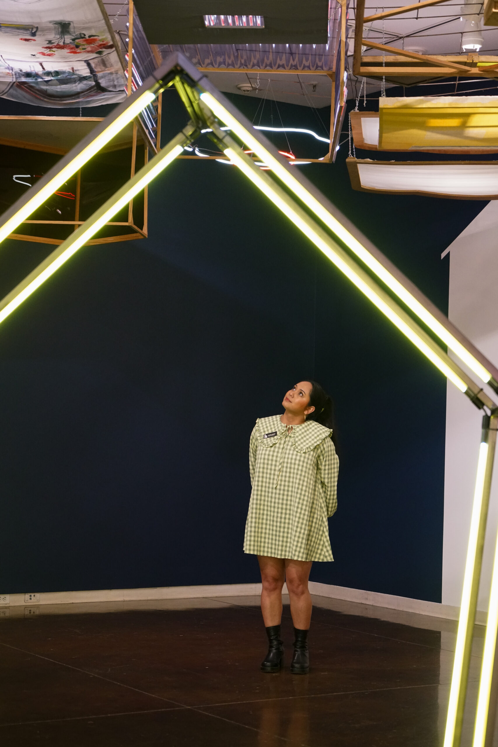 A woman in a green dress views art overhead through a neon house.