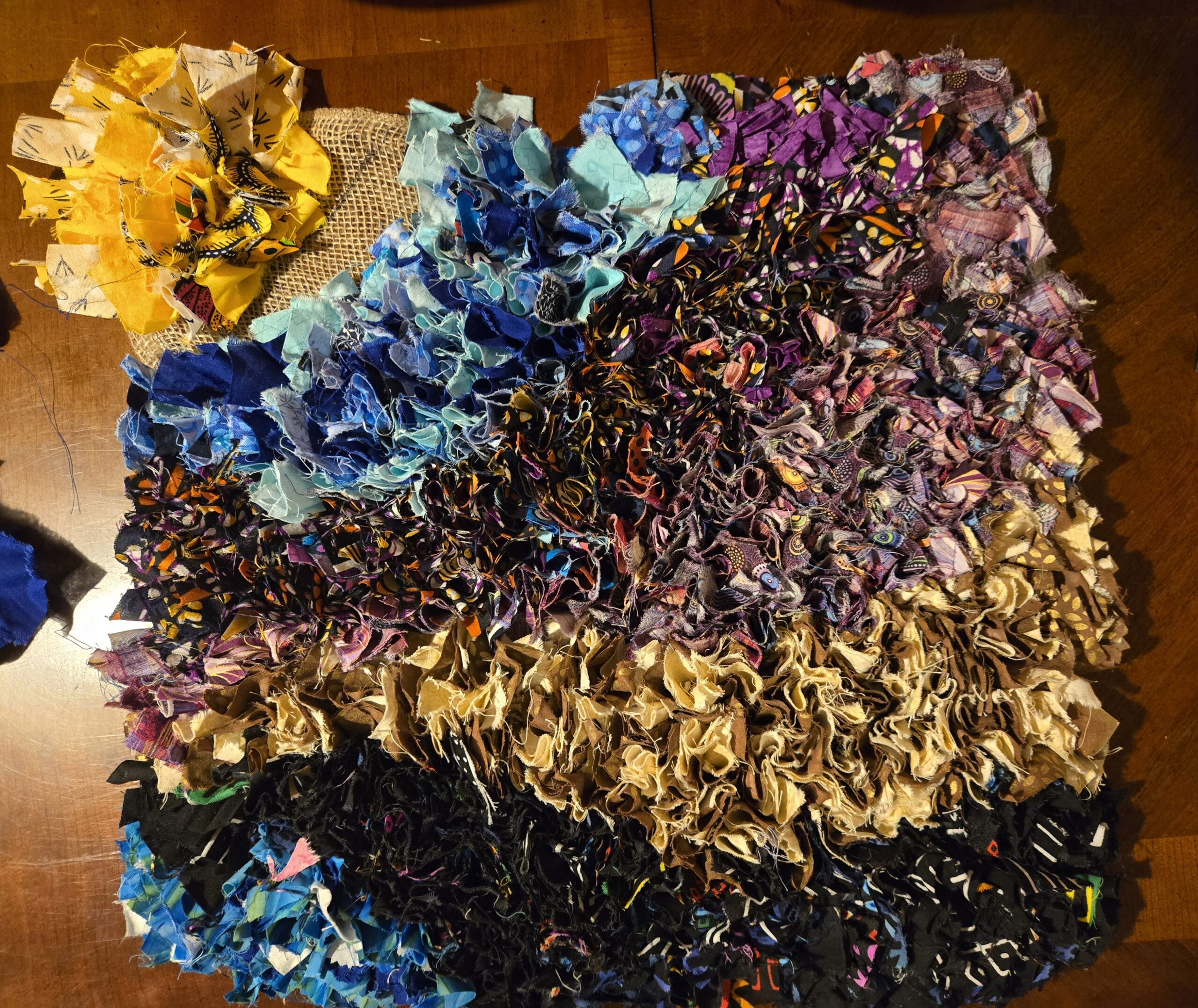A top-down view of a textured, multicolored rag quilt project on a dark wooden surface.
