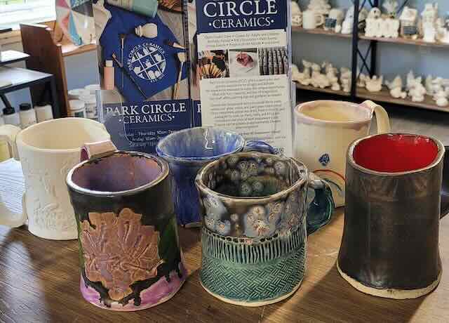 Handbuilt ceramic mugs in a studio. Some glazed in greens, blues and browns; others are unglazed.