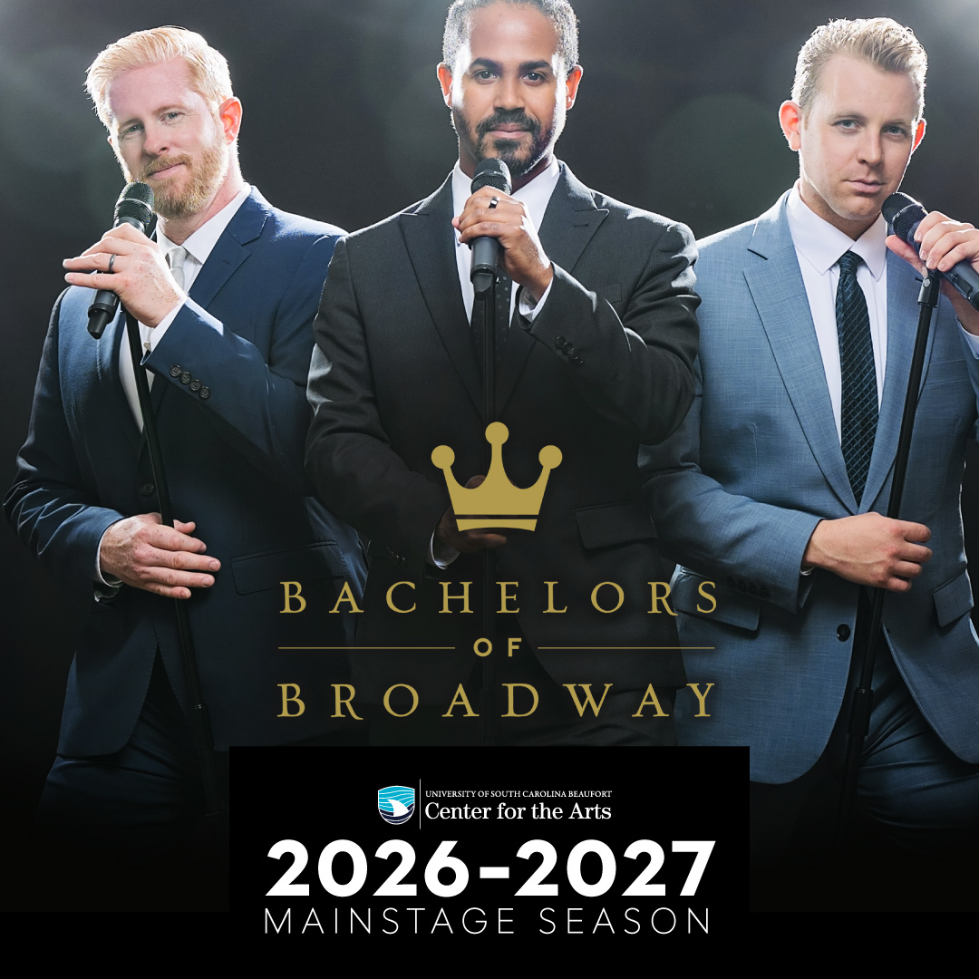 Three men in suits hold microphones under stage lights. One presents as BIPOC.