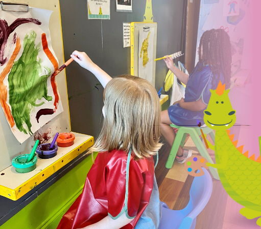 2 children, 1 BIPOC, paint at easels. A friendly cartoon dragon holds an easel and paintbrush.