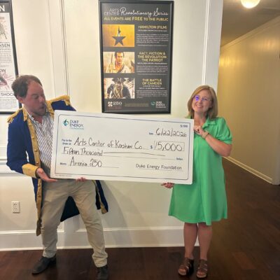 Chad Henderson from Arts Center of Kershaw County receives a mock check from a female Duke Energy representative in a bright green dress.